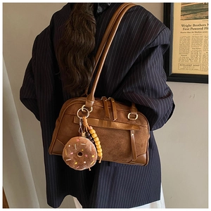 Detail of matte suede shoulder bag with plush donut charm on a striped blazer