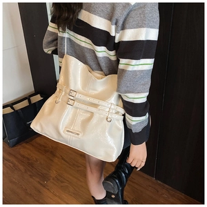 Dettaglio borsa a secchiello in pelle lucida color crema con eleganti fibbie metalliche