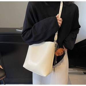 Detail of cream bucket bag with a brown teddy bear charm on model shoulder