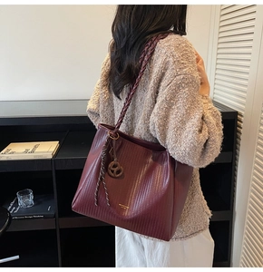 Detail of burgundy tote bag with woven texture, thick handles and pretzel charm