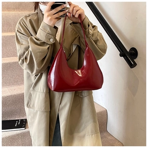 Détail du sac hobo en cuir verni bordeaux porté avec un trench-coat beige élégant
