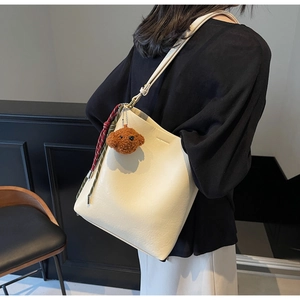 Cream bucket bag detail with plush bear charm and plaid scarf accent on a model