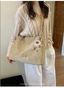 Detail of sandy beige suede tote bag featuring plush sheep pendant and brand leather tag
