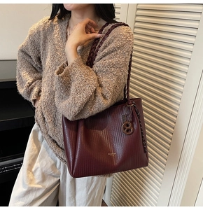 Detail of burgundy tote bag featuring woven texture and braided leather handle