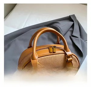 Detail view of brown leather Boston bag with stitching, dual zippers and woven pendant