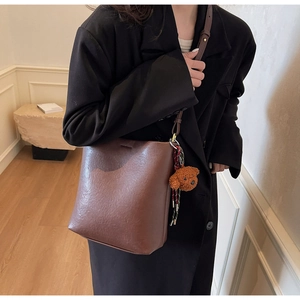 Close-up of brown leather bucket bag with a cute teddy bear pendant and thin shoulder strap