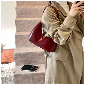 Détail du sac hobo en cuir brillant bordeaux porté par un mannequin en trench-coat