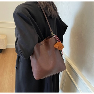 Detail of dark brown leather bucket bag with a cute plush puppy charm and slim strap