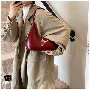 Détail d'un sac hobo en similicuir verni bordeaux porté avec un trench-coat beige