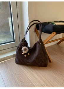 Detail of retro coffee brown suede tote bag featuring plush charm on light wood floor