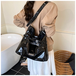 Close-up of black glossy patent leather tote bag featuring stylish double row metal buckles