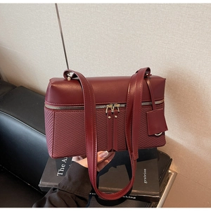 Detail of burgundy shoulder bag featuring dual zippers and woven texture panels