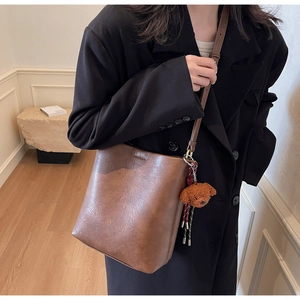 Detail of brown leather bucket bag with a cute teddy bear charm on the side
