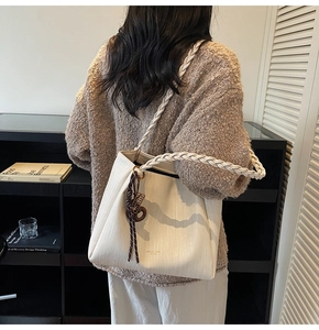 Detail of white woven texture tote bag with braided handle and brown tassel charm