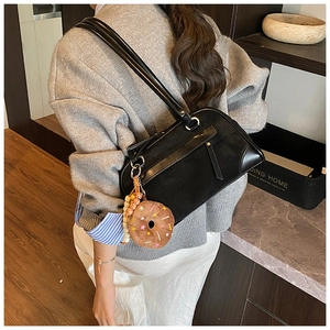 Detail of black faux leather shoulder bag with a plush donut charm and zipper closure
