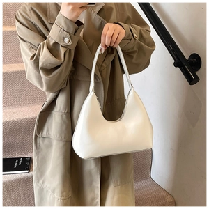 Détail d'un sac demi-lune blanc brillant porté par un mannequin en trench-coat élégant