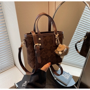 Close-up of brown suede bucket bag with diamond stitching and cute plush doll pendant