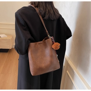 Retro brown large capacity bucket bag with cute bear charm worn over a black winter coat