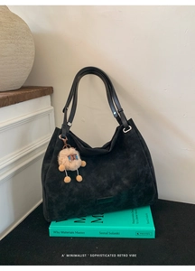 Close-up of black suede tote bag with a cute plush sheep charm on a stack of books