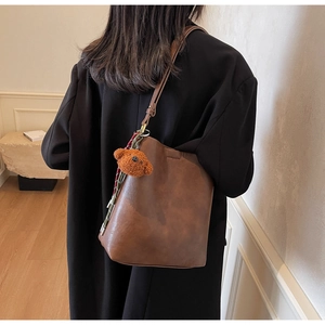 Detail of dark brown bucket bag with plush bear charm and woven lanyard on side seam