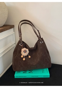 Detail of dark brown matte leather hobo bag with a plush animal pendant on green books
