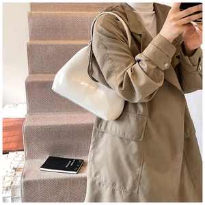 Gros plan d'un sac hobo en cuir verni blanc porté avec un trench-coat kaki élégant