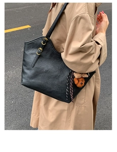 Detail einer großen schwarzen Totebag mit Teddybär-Anhänger und verstellbarer Gold-Schnalle