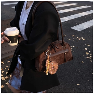 Close-up of vintage brown suede Boston bag with plush donut charm on a street