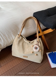 Close-up of beige matte tote bag with cute plush lamb charm on dark wood floor