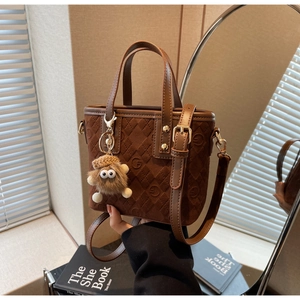 Detail of brown suede bucket bag featuring embossed patterns and cute plush charm accessory