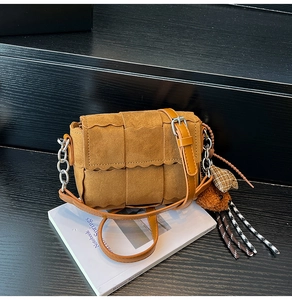Detail of woven brown shoulder bag with wavy edge flap, metal chain and bear charm