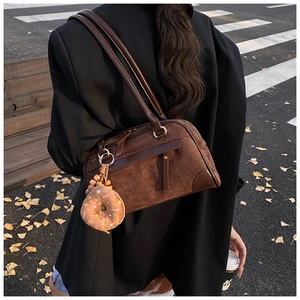 Detail of a brown suede Boston bag with leather handles and a plush donut charm decoration