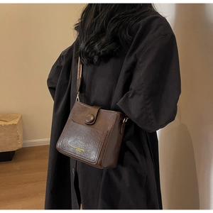 Sac seau en cuir marron à large bandoulière jacquard présenté dans un cadre intérieur