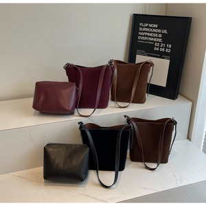 Close-up of minimalist suede bucket bags in various colors on marble display stand