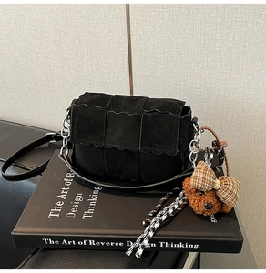 Close-up of black woven suede crossbody bag with wave edges and teddy bear charm on a book