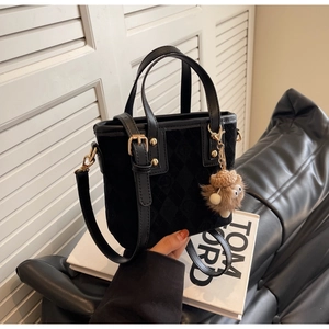 Detail of black suede bucket bag with gold hardware and brown plush doll charm