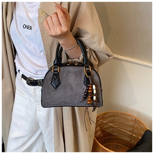 Detail of grey suede pillow bag with wooden bead charm and gold hardware on beige coat