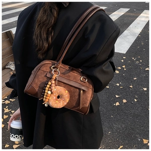Close-up of brown suede Boston bag with plush donut charm and wooden beads on shoulder