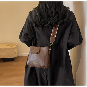 Brown leather crossbody bucket bag with wide fabric strap shown on a model