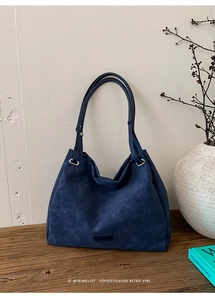 Detail of dark blue faux suede tote bag with minimalist logo patch in cozy home setting