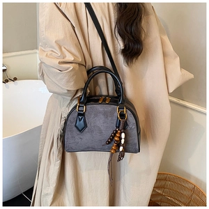 Detail shot of a grey suede crossbody bag with wood bead tassel and gold dual zippers