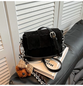 Detail of black crossbody bag with wavy flap, silver chain, and brown teddy bear charm