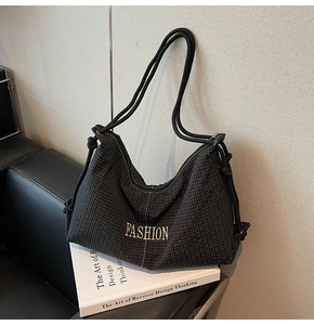 Detail view of black quilted hobo bag with gold FASHION text and decorative side knots