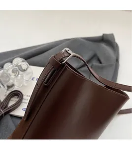 Detail of adjustable leather shoulder strap with silver buckle on a dark brown bucket bag