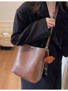 Retro brown bucket bag in textured leather with plush bear pendant shown on shoulder