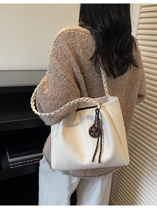 Minimalist white woven tote bag with adjustable shoulder strap and round charm detail