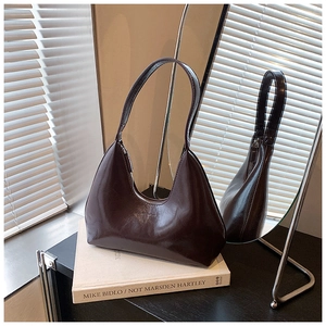 Détail d'un sac hobo marron foncé brillant posé sur des livres d'art crème en studio
