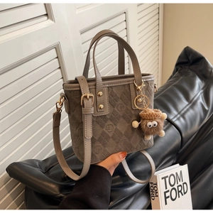 Detail of taupe frosted handbag with letter embossing and a brown plush monster charm