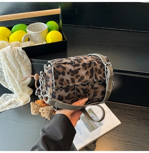Detail of leopard print woven crossbody bag with grey strap and checkered bow charm