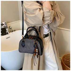 Model wearing a gray and black patchwork pillow bag with wooden bead pendant in a minimalist setting